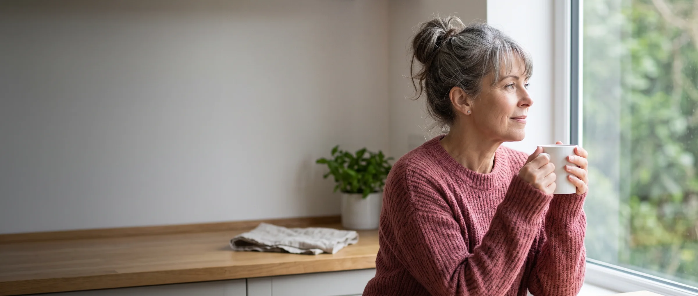 The same woman at home in the morning, rested, a mug in her hands by the window